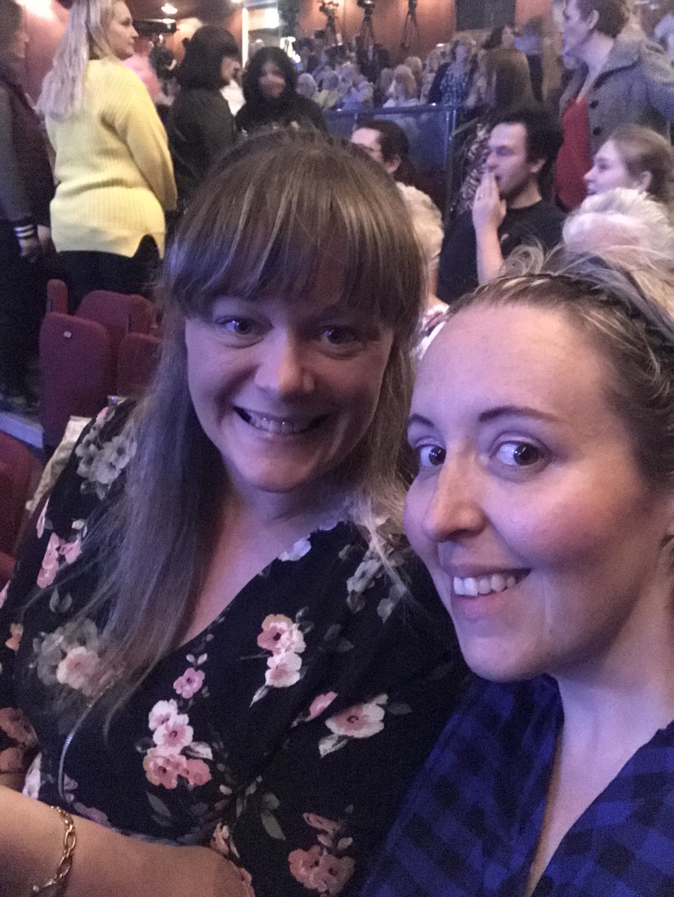 Audience gathered in a theatre background, 2 smiling ladies at the front