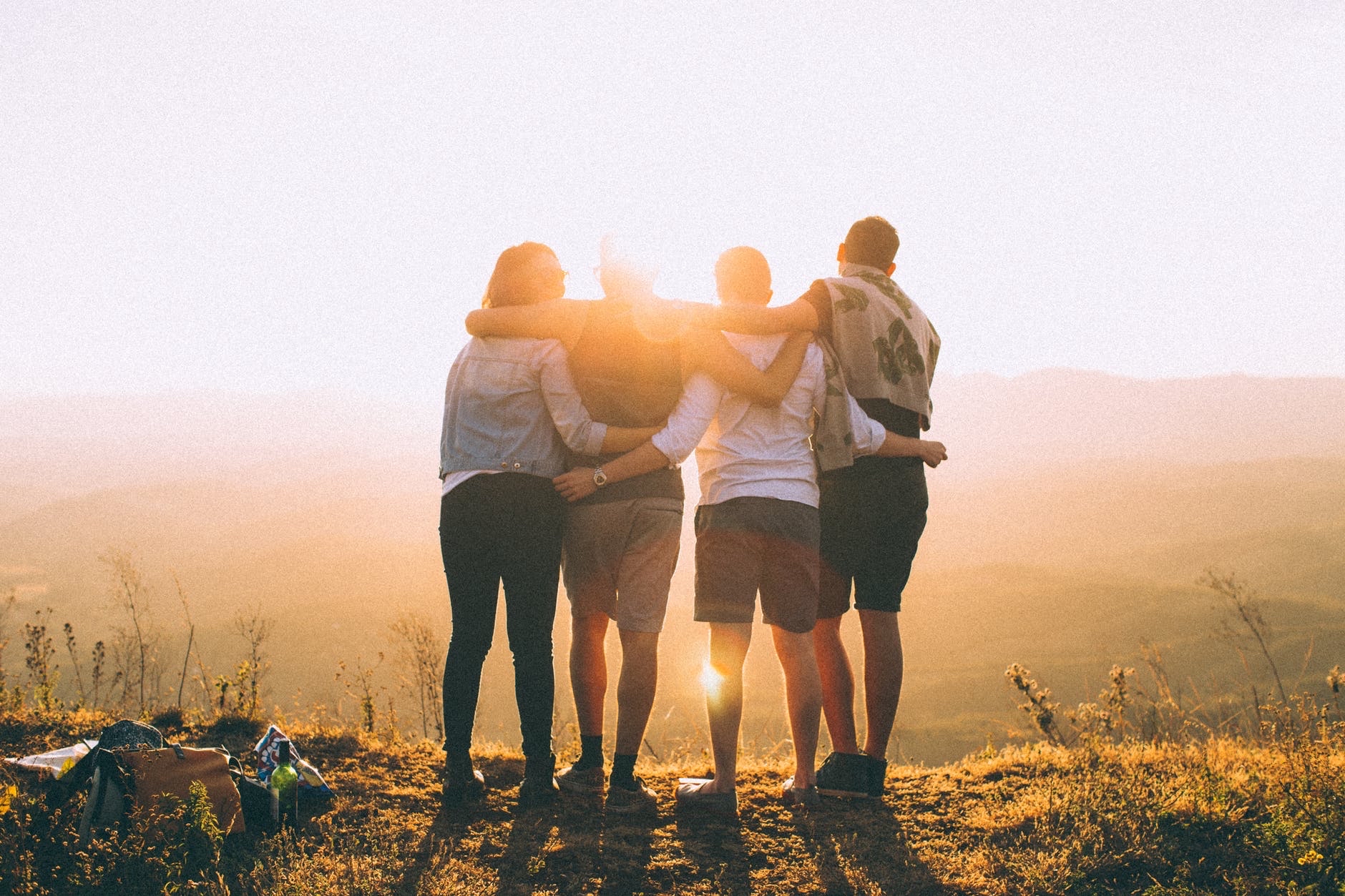 4 friends with their arms round each other looking out to sunset on mountains