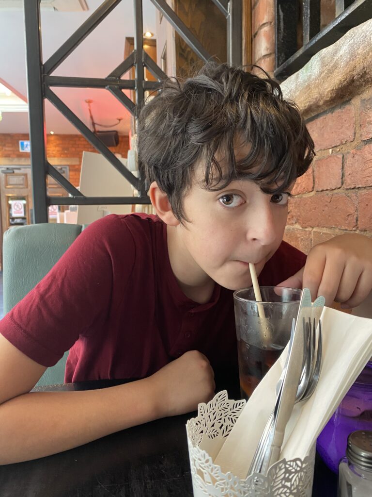 Boy in burgundy top sipping through a straw in a large drink
