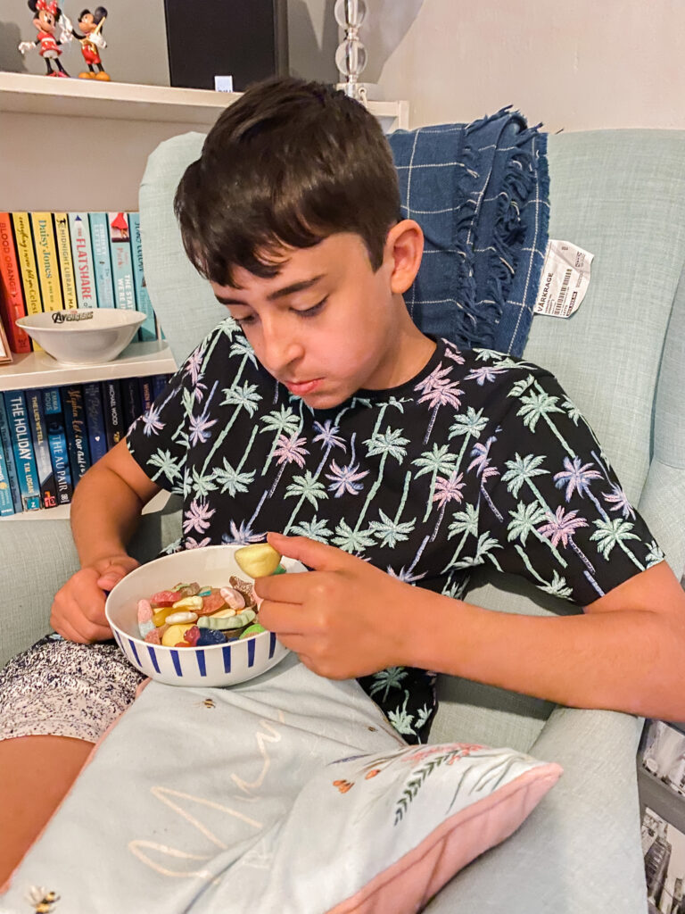 Boy sitting on a green chair eating a bowl of mixed sweets